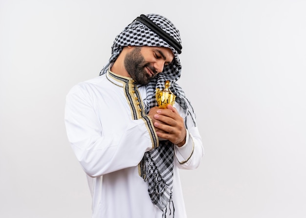 Foto gratuita uomo arabo in abbigliamento tradizionale che abbraccia il suo trofeo sorridendo sensazione di emozioni positive in piedi sopra il muro bianco