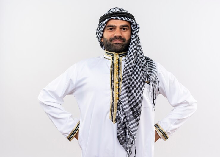 Arabic man in traditional wear with confident smile on face standing over white wall
