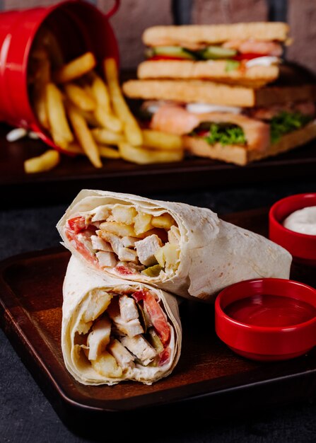 Arabic shaurma in lavash with fries and club sandwiches behind.
