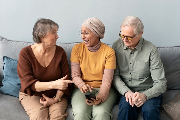 Arabic woman teaching senior couple to use smartphone sitting on sofa