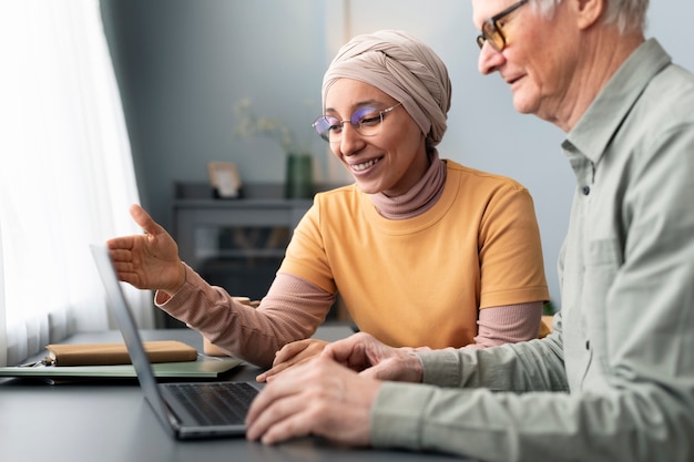 Arabic woman teaching senior man to use laptop sitting at desk