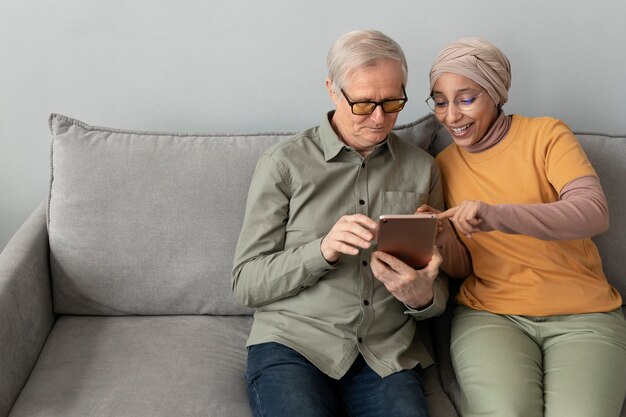 Arabic woman teaching senior man to use tablet sitting on sofa