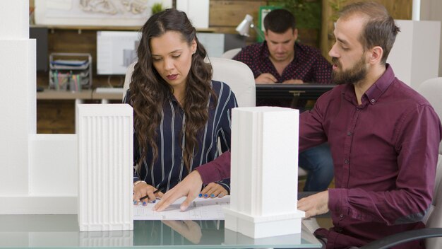 Architec and designer working with 3D printed models of buildings in modern office