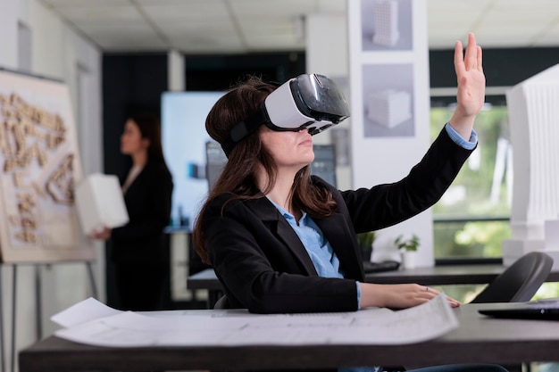 Architect in ar helmet touching virtual building model, working on project in metaverse. Employee engineering in virtual reality, real estate agency worker in vr headset in architecture office