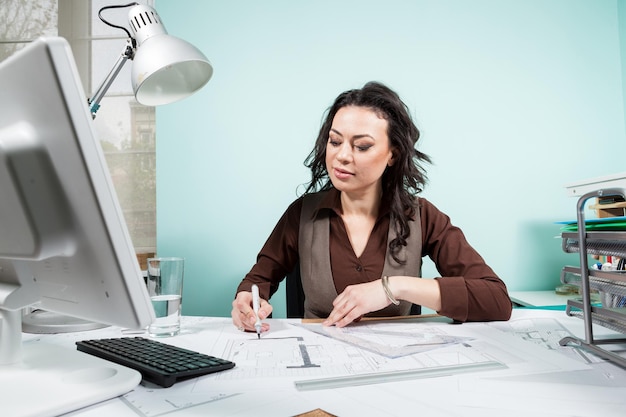 Architect at her working desk with blueprints in front of her. Working on new projects. Architecture and design