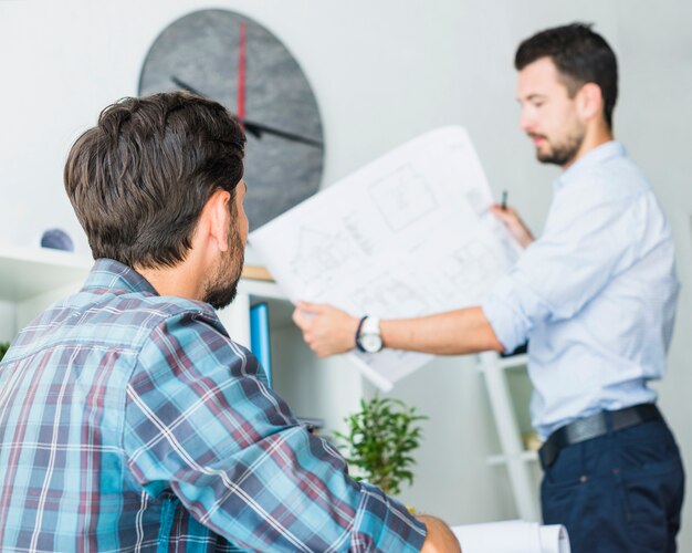 Architect looking at his colleague holding blueprint