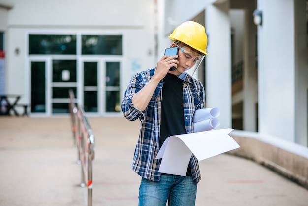 Architects hold floor plans and talk on the phone.