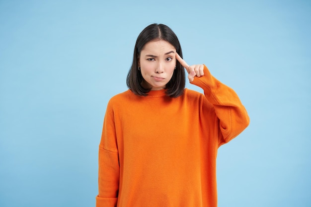 あなたは狂っていますか? 若い懐疑的なアジア人女性が誰かの行動に失望して頭の近くに指を置く