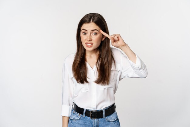 Are you dumb. Annoyed woman scolding, roll finger over head and staring at camera, bothered by someone crazy, standing over white background.