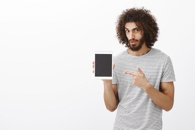 Free photo are you kidding me. portrait of unsure hesitating handsome male coworker in striped t-shirt, looking concerned while showing digital tablet