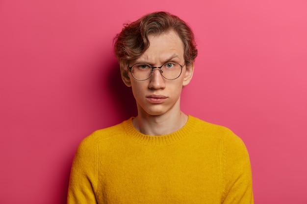 Are you serious? Strict indignant man raises eyebrows, has some doubts, being not sure, focused  with doubtful look, wears round transparent glasses and yellow jumper. Human face expressions