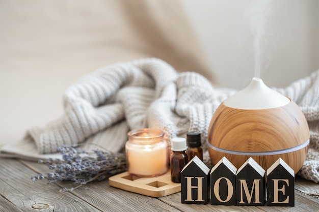 Aroma composition with modern aroma oil diffuser on wooden surface with knitted element, oils and candle on blurred background.