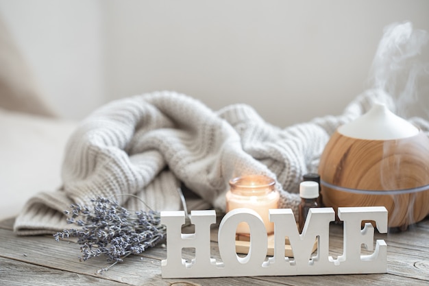 Free photo aroma composition with modern aroma oil diffuser on wooden surface with knitted element, oils and candle on blurred background