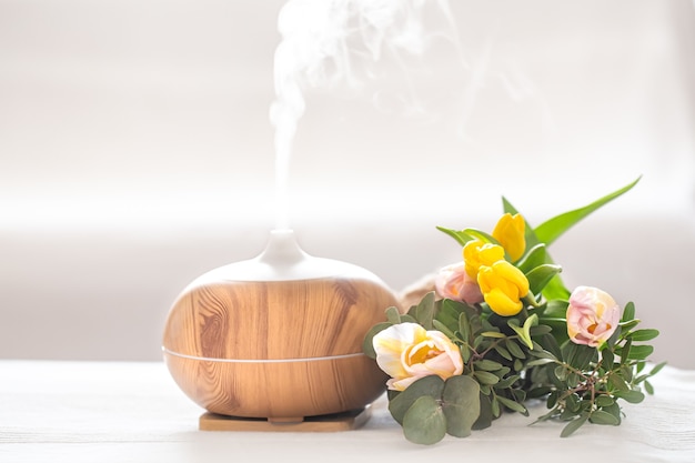 Лампа-диффузор ароматического масла на столе на размытом фоне с красивым весенним букетом тюльпанов.
