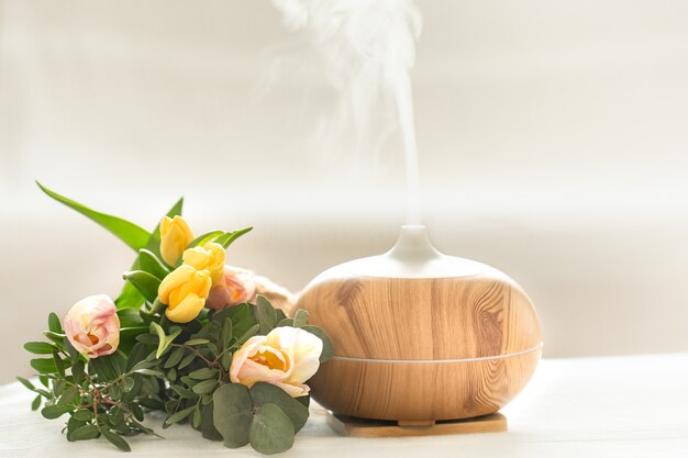 Лампа-диффузор ароматического масла на столе размыта красивым весенним букетом тюльпанов.