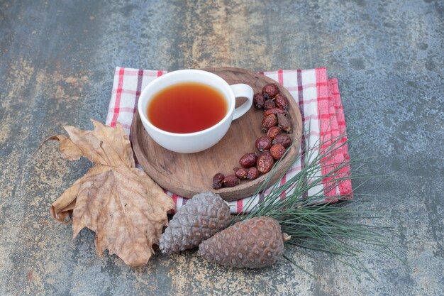 Aroma tea in white cup with rosehips and pinecones on marble background