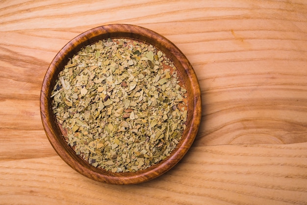 Aromatic green dry tea leaves on plate against wooden background