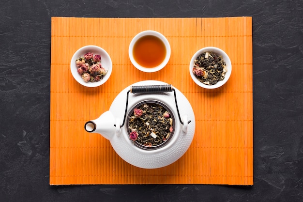 Free photo aromatic herbal tea and ingredient with white ceramic teapot on orange place mat