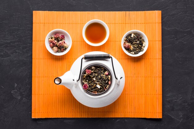 Aromatic herbal tea and ingredient with white ceramic teapot on orange place mat
