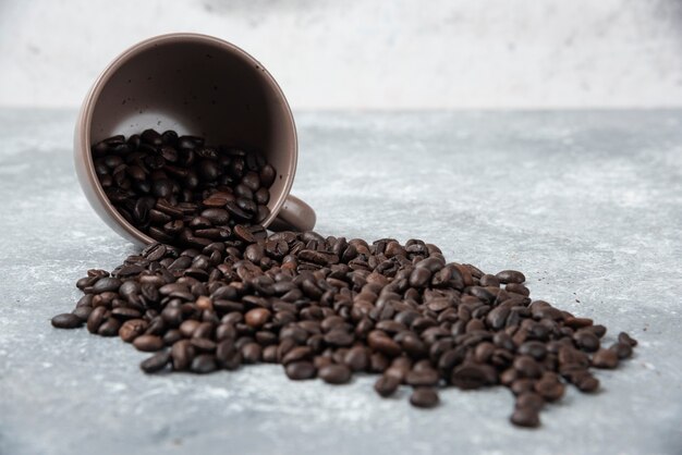 Aromatic roasted coffee beans out of cup on marble surface.