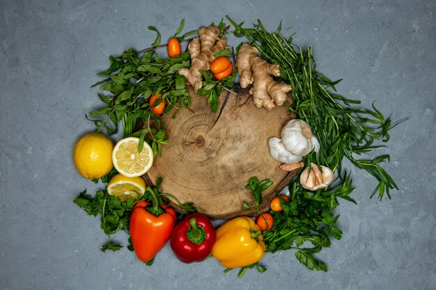 Around round wooden board set of fresh vegetables citrus and ginger on grey top view