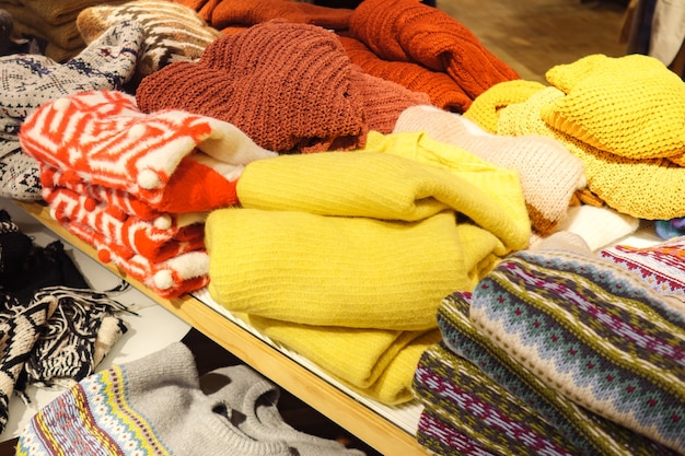 Уложенные кучи различных красочных свитеров, лежащих в беспорядке на полке внутри магазина одежды, крупным планом