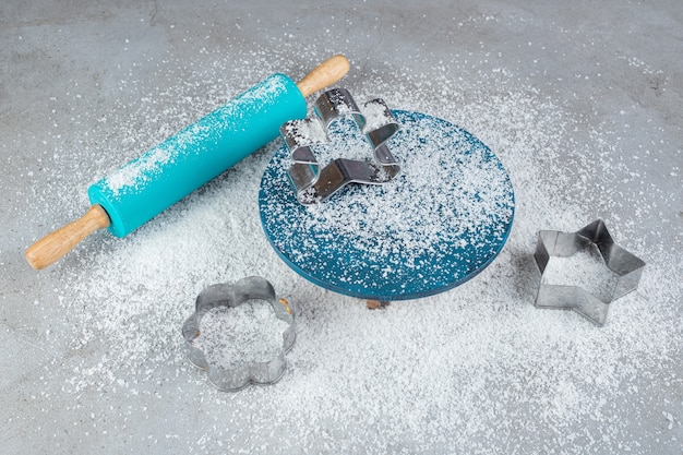 Disposizione di mattarello blu, stampi per biscotti, piatto e polvere di cocco su una superficie di marmo