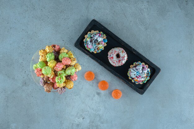 Arrangement of candied snacks with donuts, popcorns, cupcakes and jelly candies on marble surface