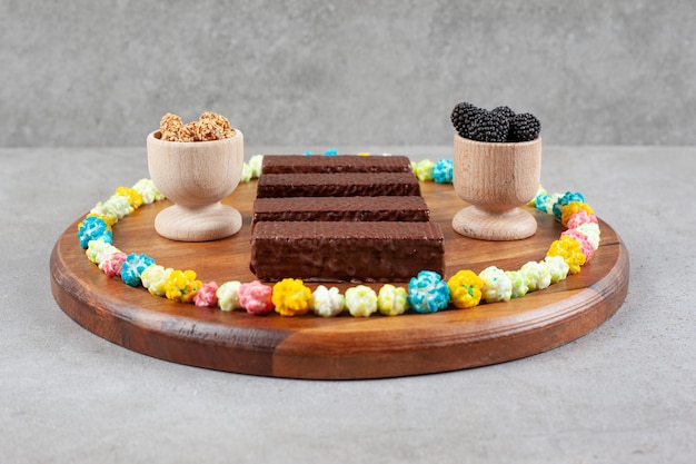 An arrangement of chocolate waffles and bowls of mullberries and glazed peanuts ringed with candy on a tray on marble surface