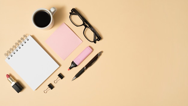 Free photo arrangement of coffee cup; eyeglass; lipstick; with office stuff on beige backdrop