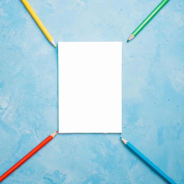青い織り目加工の表面に白い空白のカードとカラフルな鉛筆の配置
