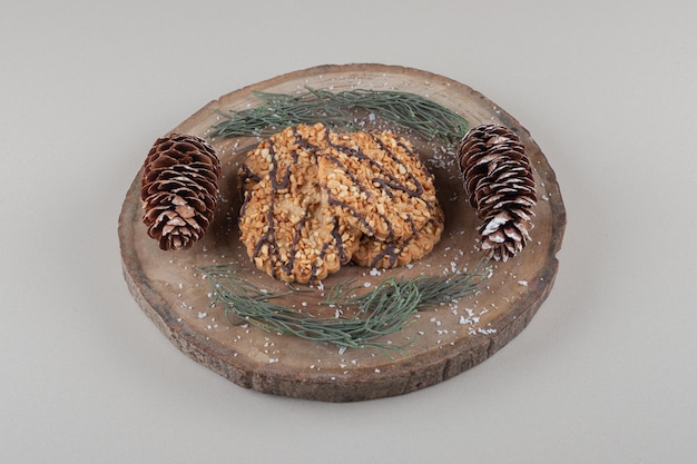Arrangement of cookies, pine cones and leaves on a wooden board on marble background.