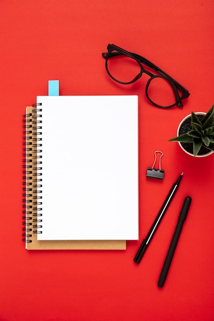 Free photo arrangement of desk elements with empty notebook on red background