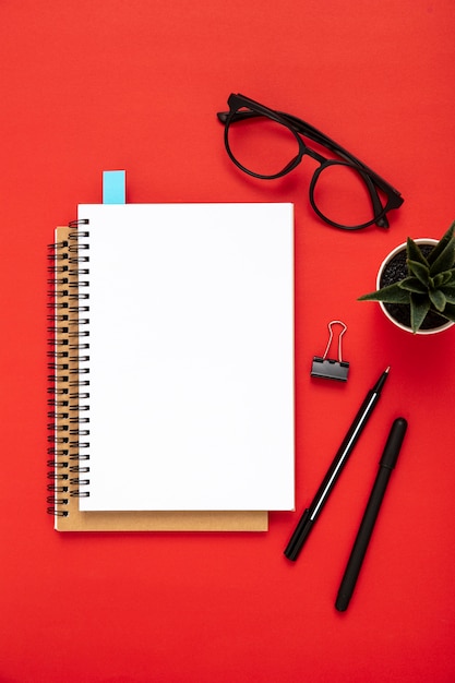 Arrangement of desk elements with empty notebook on red background