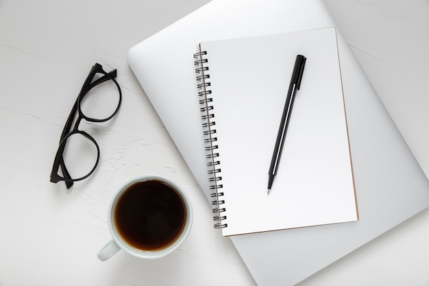 Arrangement of desk elements with empty notepad on laptop