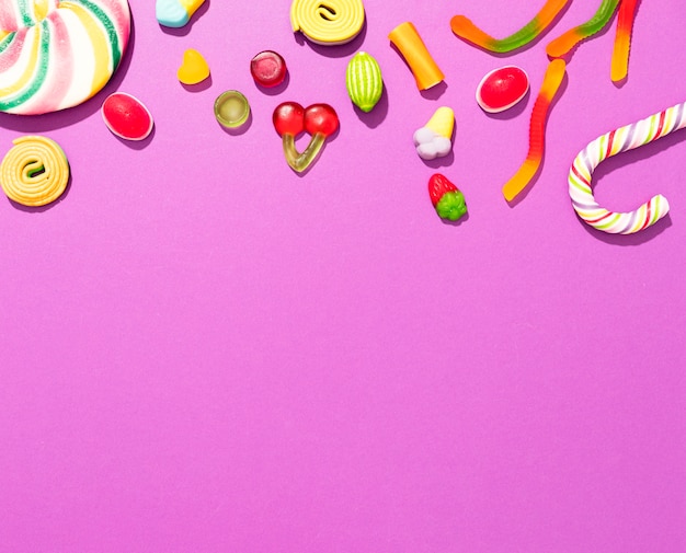 Arrangement of different colored candies on pink background with copy space