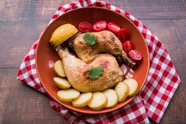 Foto gratuita arrangiamento di cosce di pollo grigliate con pomodori e patate a fette in una ciotola sopra la tovaglia