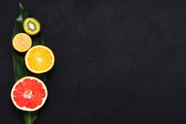 Arrangement of half of tropical fruits on banana leaf on black background