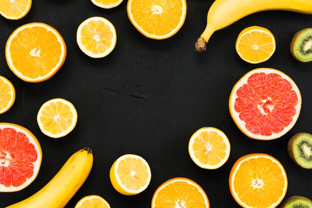 Arrangement of half of tropical fruits and whole bananas on black background