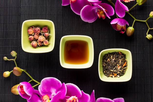 Arrangement of herbal tea and pink orchid flower over black place mat