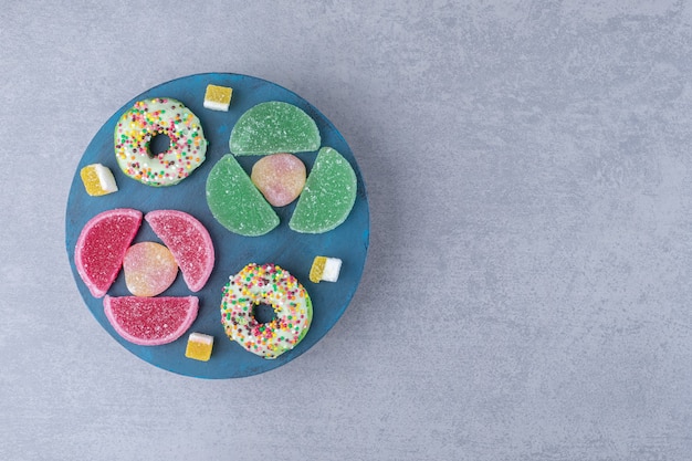 Arrangement of marmelades and donuts on a blue board on marble surface