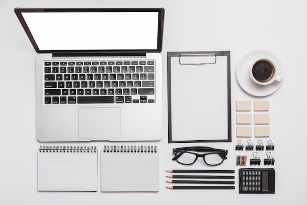 Arrangement of office desk with laptop; supplies and coffee cup