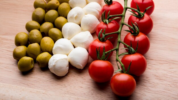 Arrangement of red cheery tomatoes; cheese; olives over wooden surface