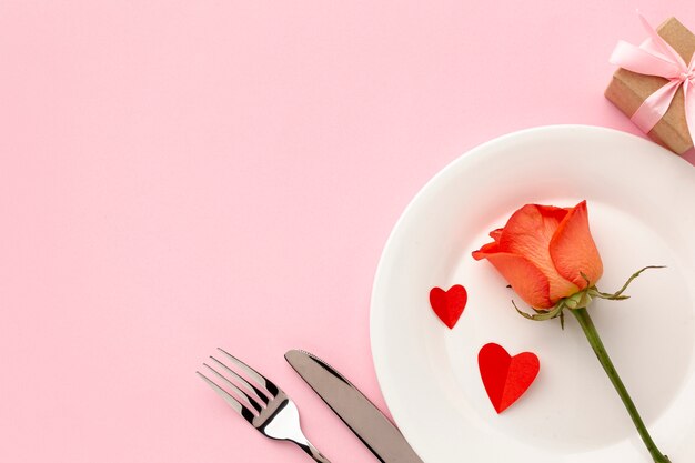 Arrangement for valentine's day dinner on pink background with orange rose