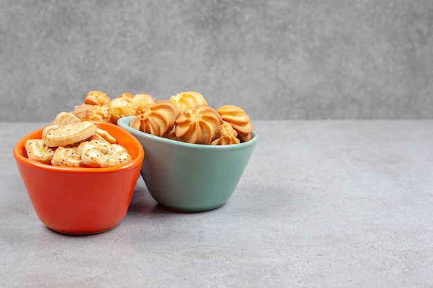 Arrangement of various biscuits and cookies in colorful bowls on marble background. 