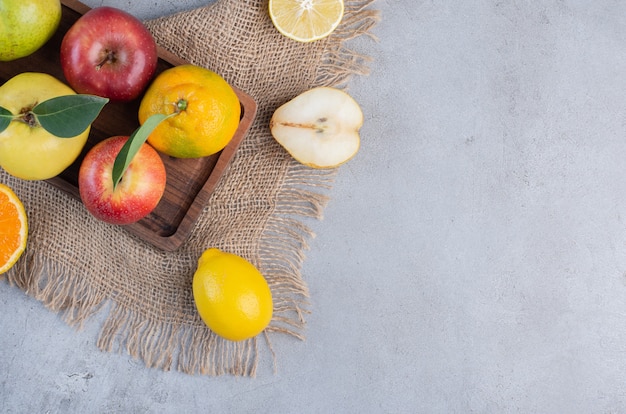 An arrangement of various fruits on a wooden board and a piece of cloth on marble background. 