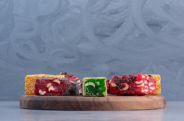 An arrangement of various Turkish delight flavors on a wooden board on marble background.