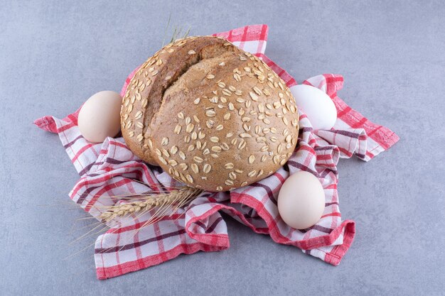 Arrangement of wheat stalks, eggs and a loaf of bread on a towel on marble surface