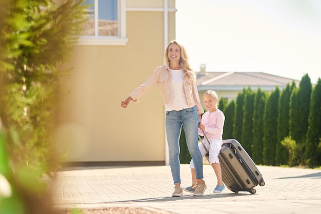 Arrival. Blonde woman carrying a suitcase with her daughter riding it