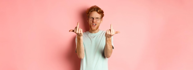 Foto gratuita un uomo dai capelli rossi arrogante e maleducato con gli occhiali se ne frega un cazzo mostrando il dito medio alla telecamera e accigliato